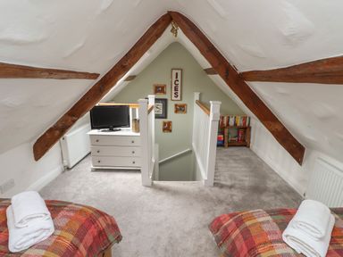 An attic bedroom with exposed wooden beams two beds with folded towels a white dresser with a television and a bookshelf at Lark Rise in Alnmouth