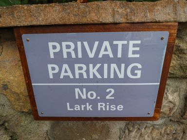 A sign on a stone wall reading private parking No 2 Lark Rise