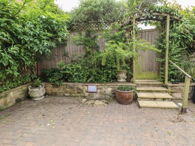 A paved parking area with stone steps leading to a wooden gate surrounded by plants and a wooden fence at Lark Rise in Alnmouth