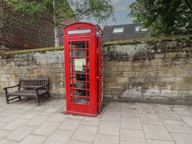 A red telephone booth next to a wooden bench against a stone wall outdoors
