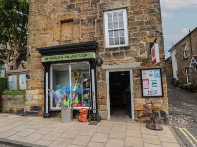 The exterior of Alnmouth Village Store with a display window and an open door on a stone building in Alnmouth