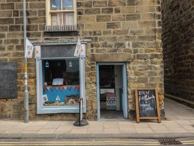 A stone building with a shop window and an open door with signs advertising crab sandwiches and gelato at Lark Rise in Alnmouth