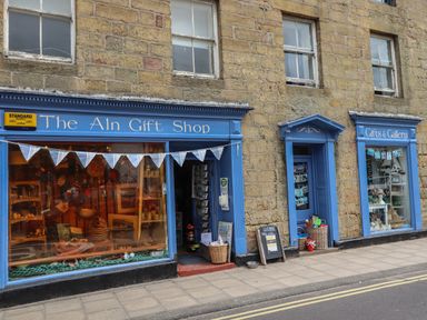 A stone building with blue framed gift shop and gallery windows on a street at Lark Rise in Alnmouth