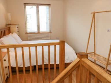 A bedroom with a wooden bed white bedding a wooden chest of drawers and a wooden clothes rack at The Loft Cottage in Totnes
