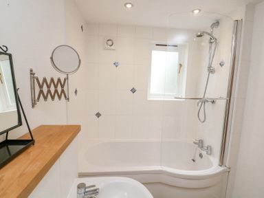 A bathroom with bathtub shower combination window and sink with a wooden shelf at The Loft Cottage in Totnes