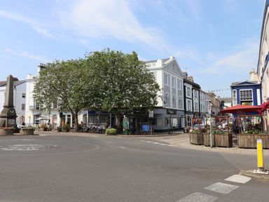 A town square with trees white buildings outdoor seating and pedestrians at The Loft Cottage in Totnes