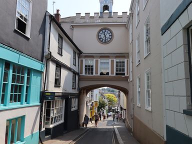 A street with a clock tower over an archway and people walking at The Loft Cottage in Totnes