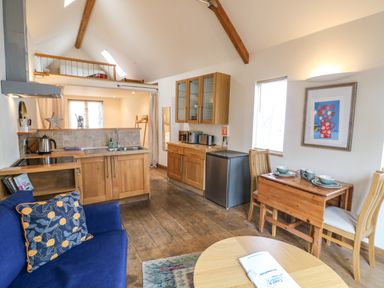 A small kitchen and dining area with wooden cabinets a blue sofa and a loft space at The Loft Cottage in Totnes