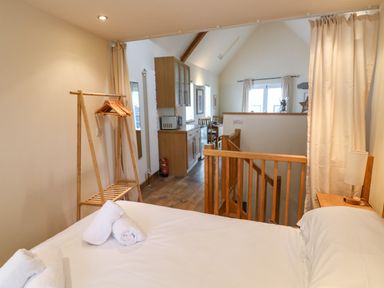 A bedroom with a bed towels wooden clothes rack and a view into a kitchen and dining area at The Loft Cottage in Totnes
