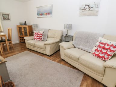 A living room with two beige sofas and red patterned cushions at Badger Sett in Granite Henge near Looe