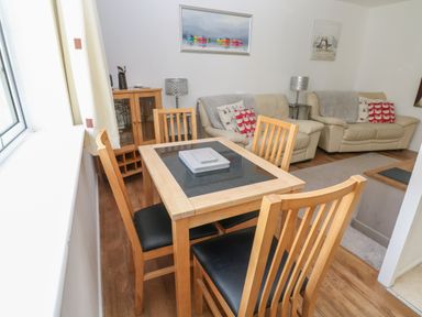 A dining area with wooden table and chairs next to a living room with two sofas and cushions at Badger Sett in Granite Henge near Looe