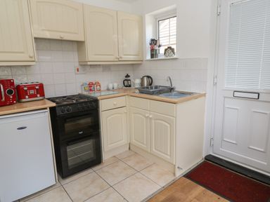 A kitchen with cream cabinets a black oven a white mini fridge a red toaster and kettle at Badger Sett in Granite Henge near Looe