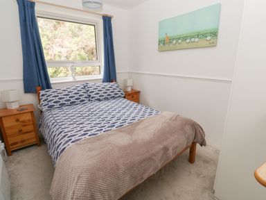 A bedroom with a double bed blue curtains wooden side tables and a painting on the wall at Badger Sett in Granite Henge near Looe