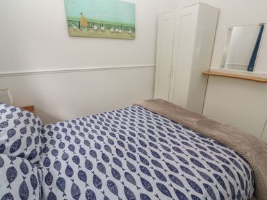 A bedroom with a bed with fish patterned bedding a white wardrobe a wall mirror and a painting on the wall at Badger Sett in Granite Henge near Looe