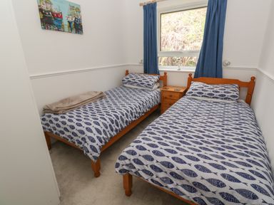 A bedroom with two single beds with blue fish patterned bedding a wooden nightstand between them and blue curtains at the window at Badger Sett in Granite Henge near Looe