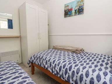 A bedroom with two single beds with fish patterned bedding a white wardrobe a folded blanket and a painting of boats on the wall at Badger Sett in Granite Henge near Looe near Polperro