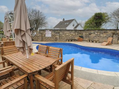 An outdoor swimming pool with wooden tables chairs and closed umbrellas at Badger Sett in Granite Henge near Looe