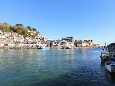 A harbor with boats docked next to a pier and houses on a hillside at Badger Sett in Granite Henge near Looe in Looe near Polperro