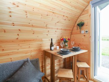 A small wooden dining table set with plates glasses and a bottle of wine next to a sofa and an open door at Nebo Pod in Amlwch