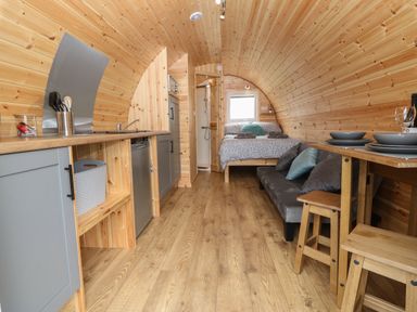 An interior of a wooden pod with a kitchen area a bed a couch and a dining table at Nebo Pod in Amlwch
