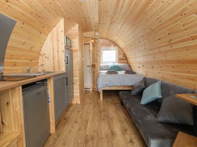 A compact wooden pod interior with a bed a small kitchenette and a sofa at Nebo Pod in Amlwch