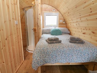 A bedroom with a bed with folded towels and a rounded shower enclosure in a wooden pod at Nebo Pod in Amlwch