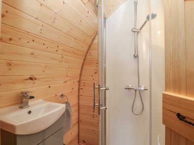 A bathroom with wooden panel walls a white sink a gray cabinet a hand towel and a shower at Nebo Pod in Amlwch