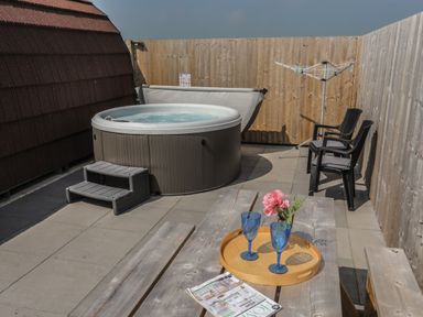An outdoor patio area with a hot tub steps wooden picnic table with tray and glasses two black chairs and a wooden fence at Nebo Pod in Amlwch