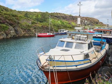 Several boats docked in a small harbor with rocky hills and vegetation in the background at Nebo Pod in Amlwch