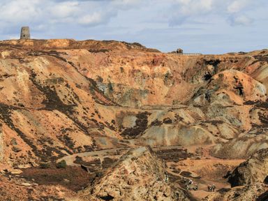 A rocky landscape with scattered vegetation and workers in safety gear at Nebo Pod in Amlwch