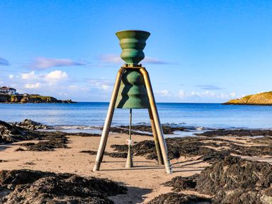 A beach with rocky patches and a metal sculpture near the shore
