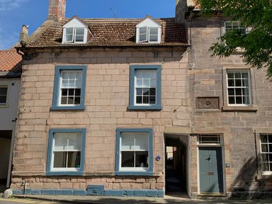 Exterior of a stone house with blue window frames and a green door beside an alleyway at The Indigo House in Berwick-Upon-Tweed
