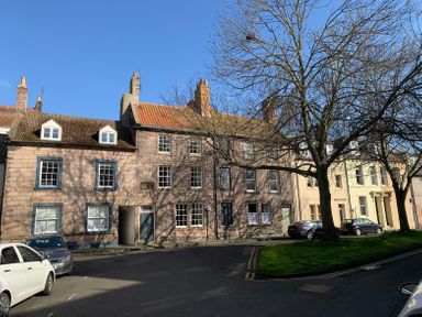 A street with rows of traditional houses with chimneys and parked cars along a road with a tree in the foreground at The Indigo House in Berwick-Upon-Tweed