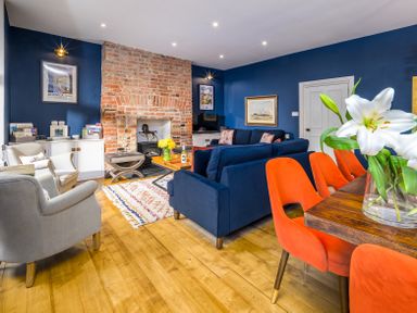 A living room with blue walls a brick fireplace blue sofas orange chairs and wooden floor at The Indigo House in Berwick-Upon-Tweed