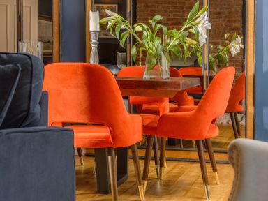 A dining area with orange chairs around a wooden table and white flowers in a vase at The Indigo House in Berwick-Upon-Tweed