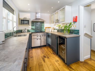 A kitchen with stainless steel oven, green tiled backsplash, wooden floor and flowers in a vase on the countertop at The Indigo House in Berwick-Upon-Tweed