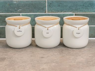 Three white ceramic jars with wooden lids labeled coffee tea and sugar on a countertop with teal tile backsplash at The Indigo House in Berwick-Upon-Tweed