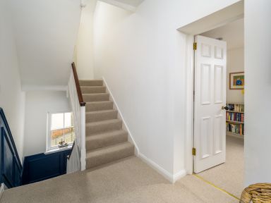 A carpeted staircase with a wooden handrail and a partially open white door leading to a room with bookshelves at The Indigo House in Berwick-Upon-Tweed