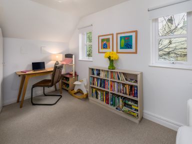 A study room with a desk laptop chair lamp bookshelf with books and flowers at The Indigo House in Berwick-Upon-Tweed