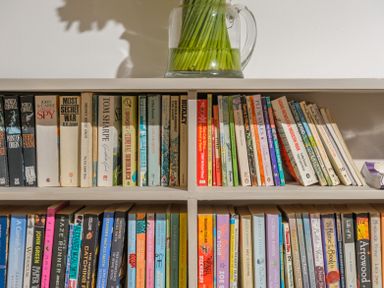 Shelf with two rows of assorted books and a glass jug with green plant stems on top at The Indigo House in Berwick-Upon-Tweed