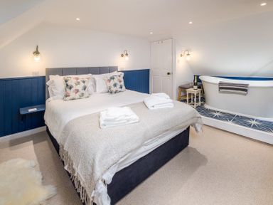 A bedroom with a bed towels and a bathtub on a platform at The Indigo House in Berwick-Upon-Tweed