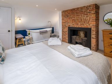 A bedroom with a bed folded towels a brick fireplace freestanding bathtub and wooden dresser at The Indigo House in Berwick-Upon-Tweed