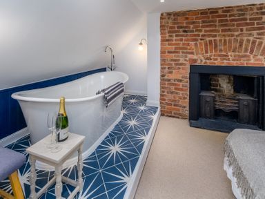A bathroom with a white freestanding bathtub on blue patterned tiles and a brick fireplace at The Indigo House in Berwick-Upon-Tweed