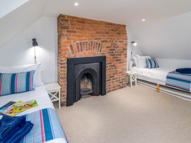 A bedroom with two single beds a brick fireplace and bedside tables at The Indigo House in Berwick-Upon-Tweed