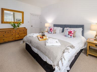 A bedroom with a bed with floral pillows a wooden dresser with a mirror and bedside tables with lamps at The Indigo House in Berwick-Upon-Tweed