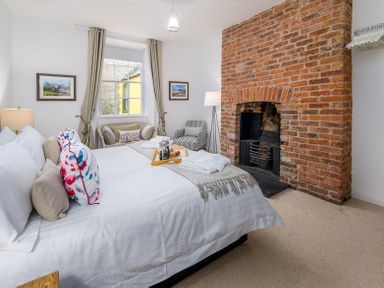 A bedroom with a bed pillows a brick fireplace a window with curtains and two chairs at The Indigo House in Berwick-Upon-Tweed