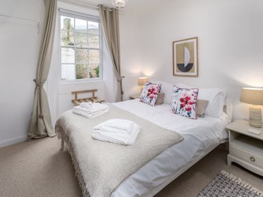 A bedroom with a double bed with floral pillows bedside tables with lamps and a window with curtains at The Indigo House in Berwick-Upon-Tweed