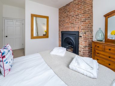 A bedroom with a bed folded towels a wooden dresser and a brick fireplace at The Indigo House in Berwick-Upon-Tweed