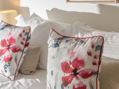 Two floral patterned pillows on a bed with white sheets and a lamp in the background at The Indigo House in Berwick-Upon-Tweed