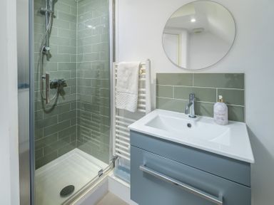 A bathroom with a shower, towel rail, sink, and round mirror at The Indigo House in Berwick-Upon-Tweed